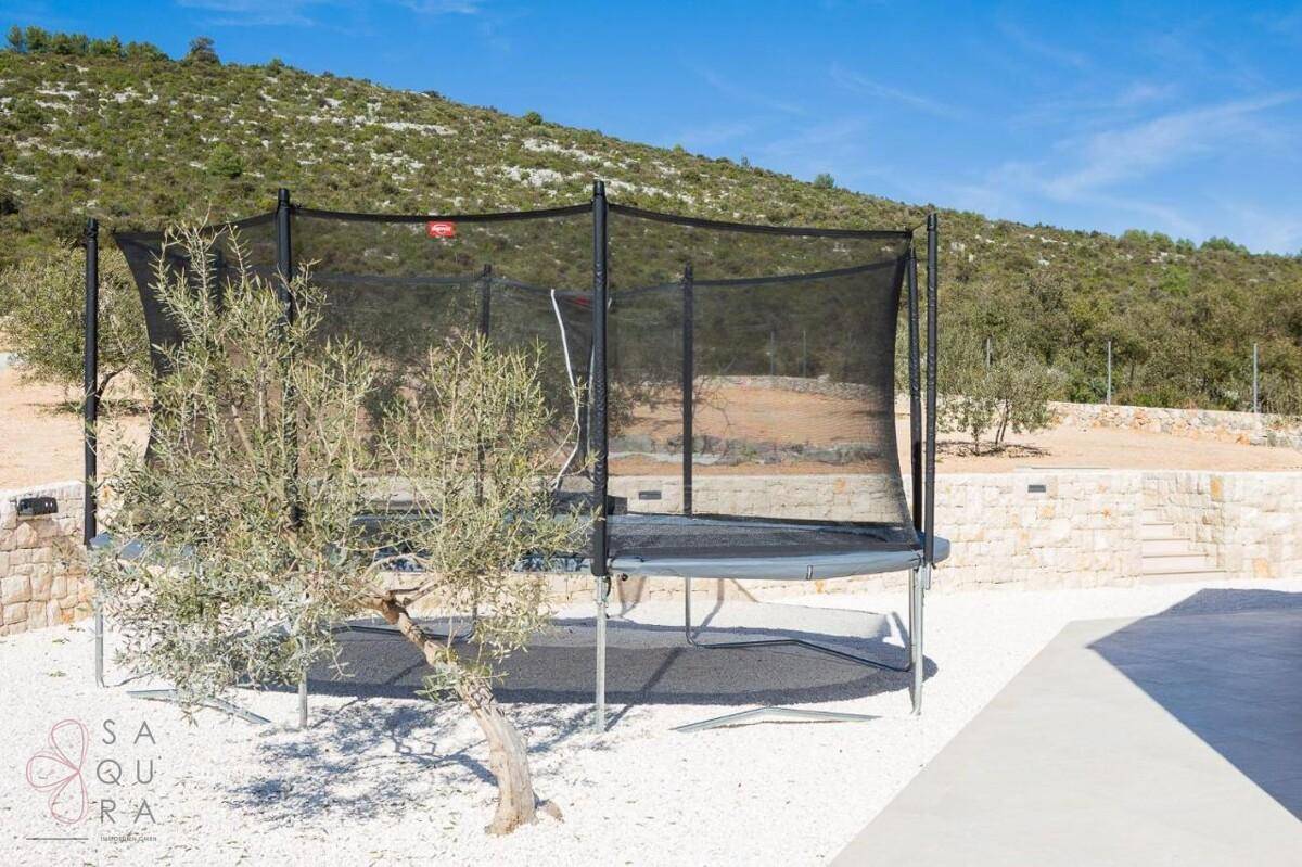Großer Trampolin im Gartenbereich, umgeben von mediterraner Bepflanzung und Steinmauern.
