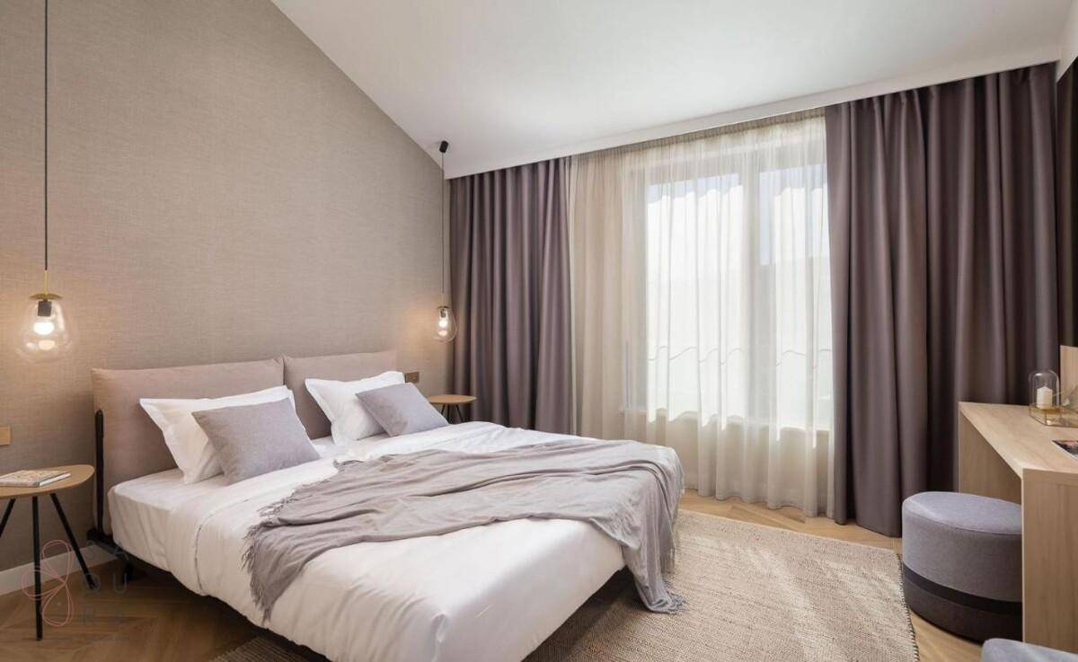 Helles Schlafzimmer mit Doppelbett, großem Fenster und Blick auf die umliegende Natur.