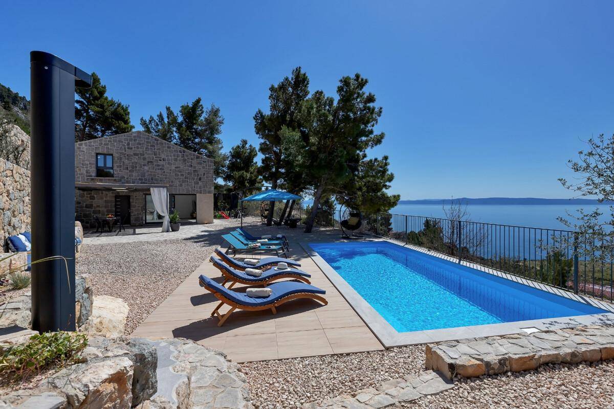 Sonniger Poolbereich mit bequemen Liegestühlen und weitem Blick auf das glitzernde Meer.