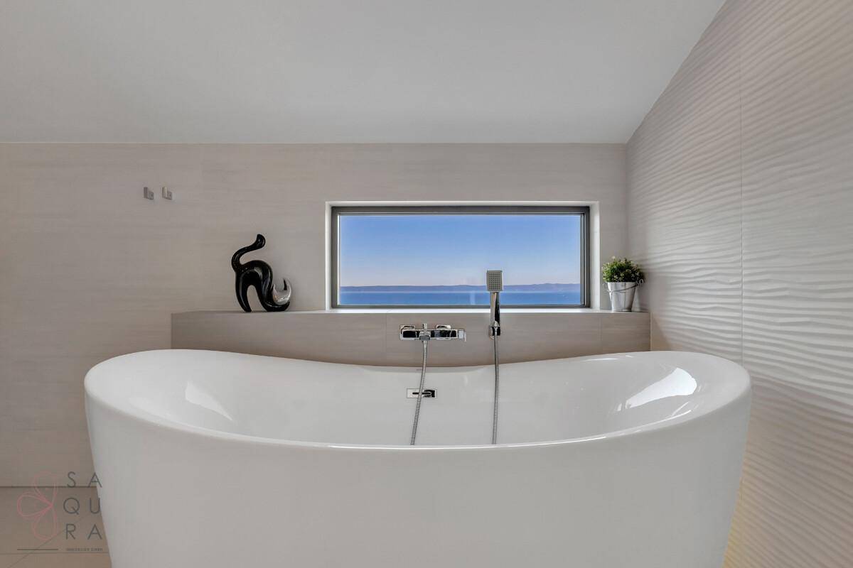 Modernes Badezimmer mit freistehender Badewanne und einem Fenster mit Meerblick.
