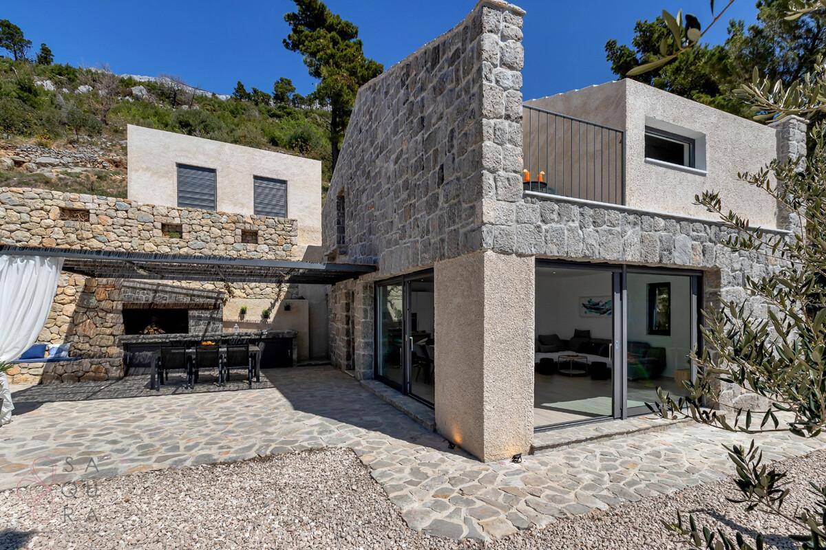 Attraktive Steinfassade mit überdachter Terrasse und Außenküche, ideal für Mahlzeiten im Freien.