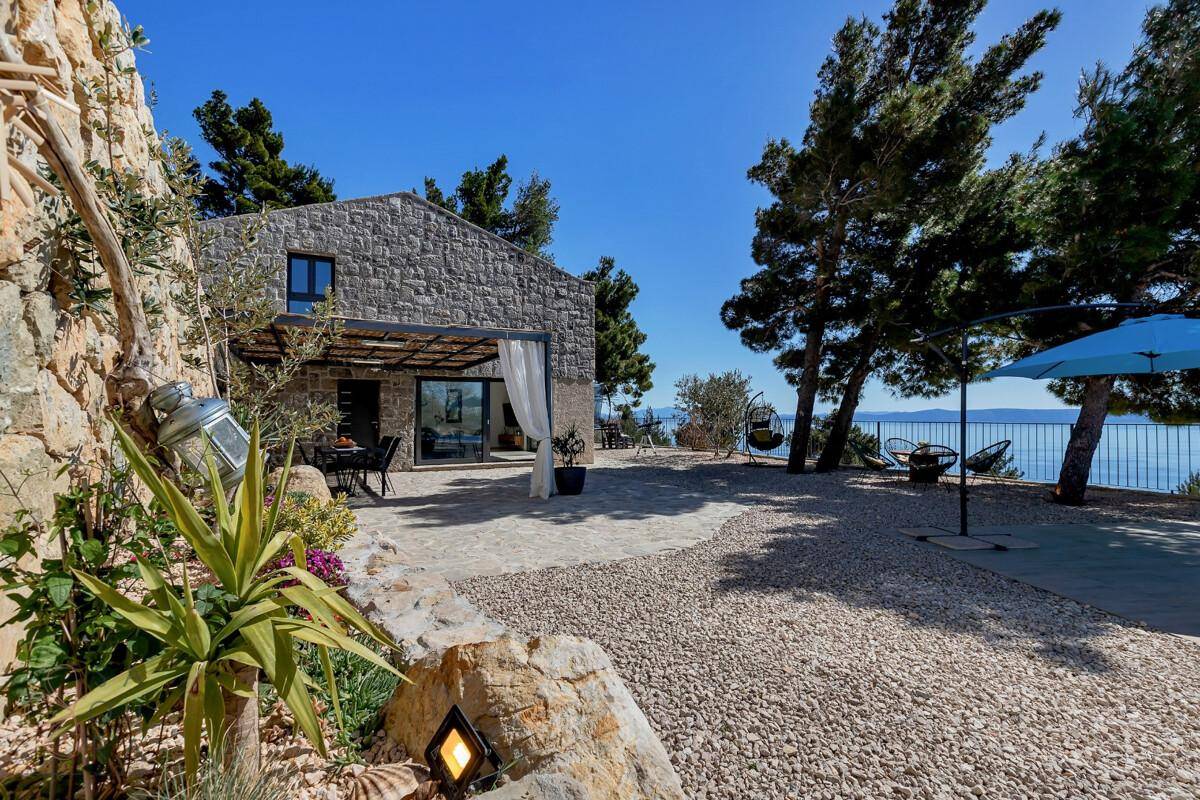 Mediterraner Gartenbereich mit Kieswegen, Pflanzen und einem charmanten Steinhaus im Hintergrund.