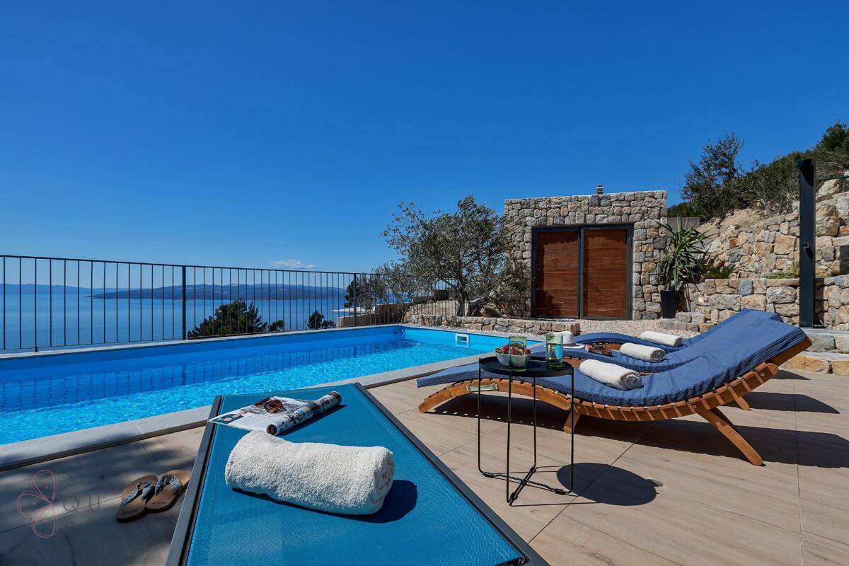 Entspannender Poolbereich mit Liegestühlen und weitem Blick auf das Meer und die Küste.