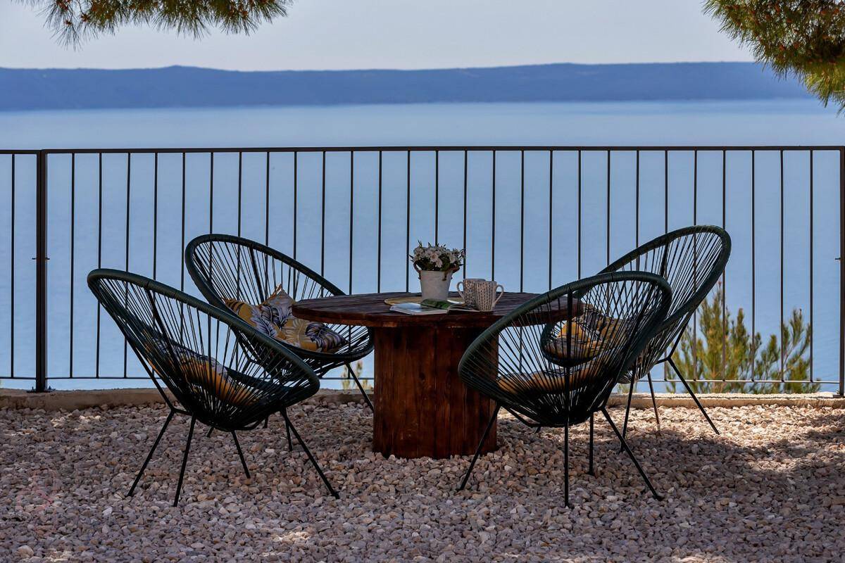 Gemütlicher Sitzbereich im Freien mit modernen Stühlen und Tisch, umgeben von Kies und Meerblick.