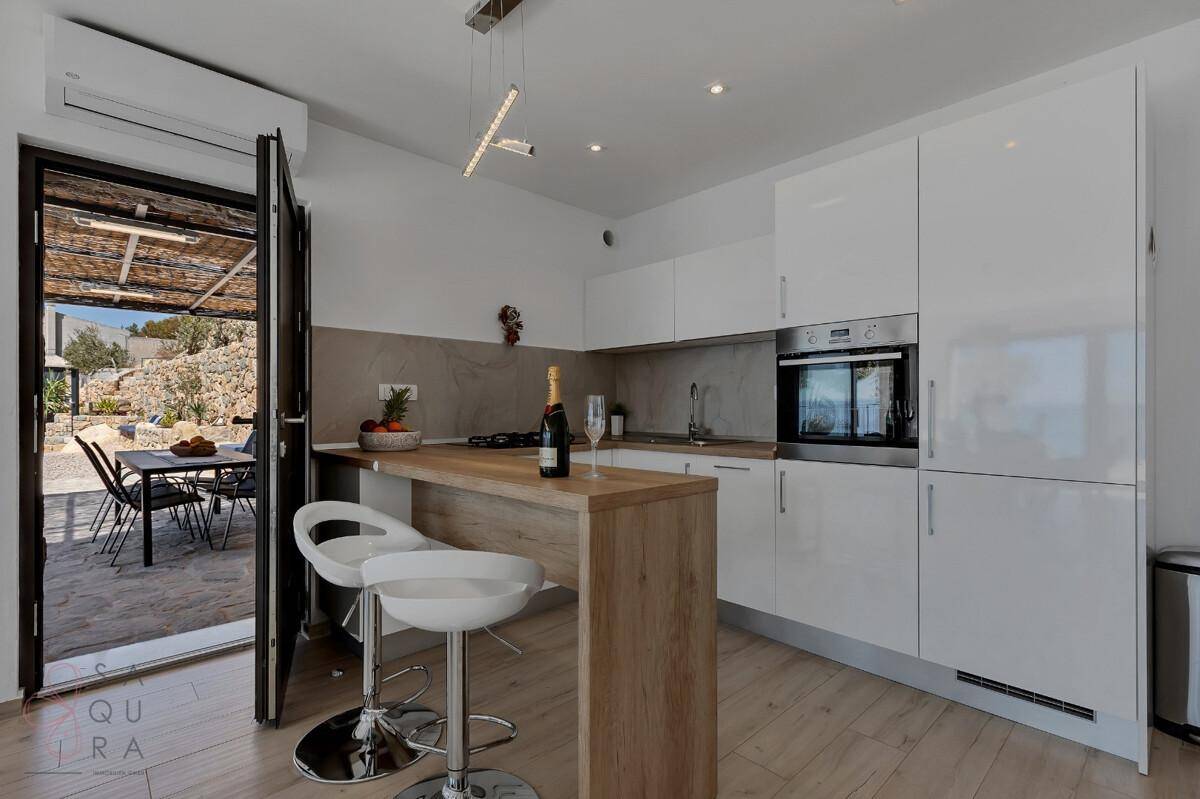 Moderne Küche mit weißen Hochglanzfronten, Holzarbeitsplatte und Frühstücksbar mit Zugang zur Terrasse.