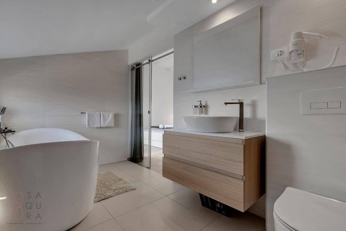 Modernes Badezimmer mit freistehender Badewanne, Waschtisch und Spiegel, hell und geräumig.