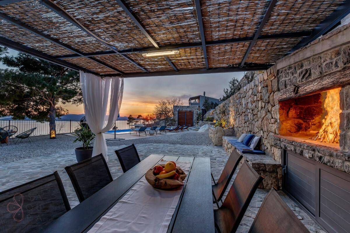 Überdachter Essbereich im Freien mit Kamin und Blick auf den Pool und den Sonnenuntergang über dem Meer.