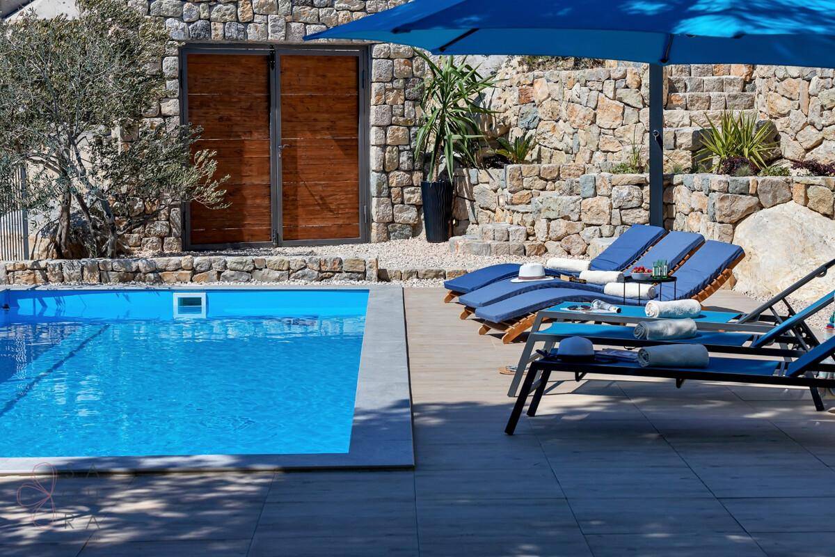 Sonniger Poolbereich mit Liegestühlen und blauem Sonnenschirm, ideal zum Entspannen.