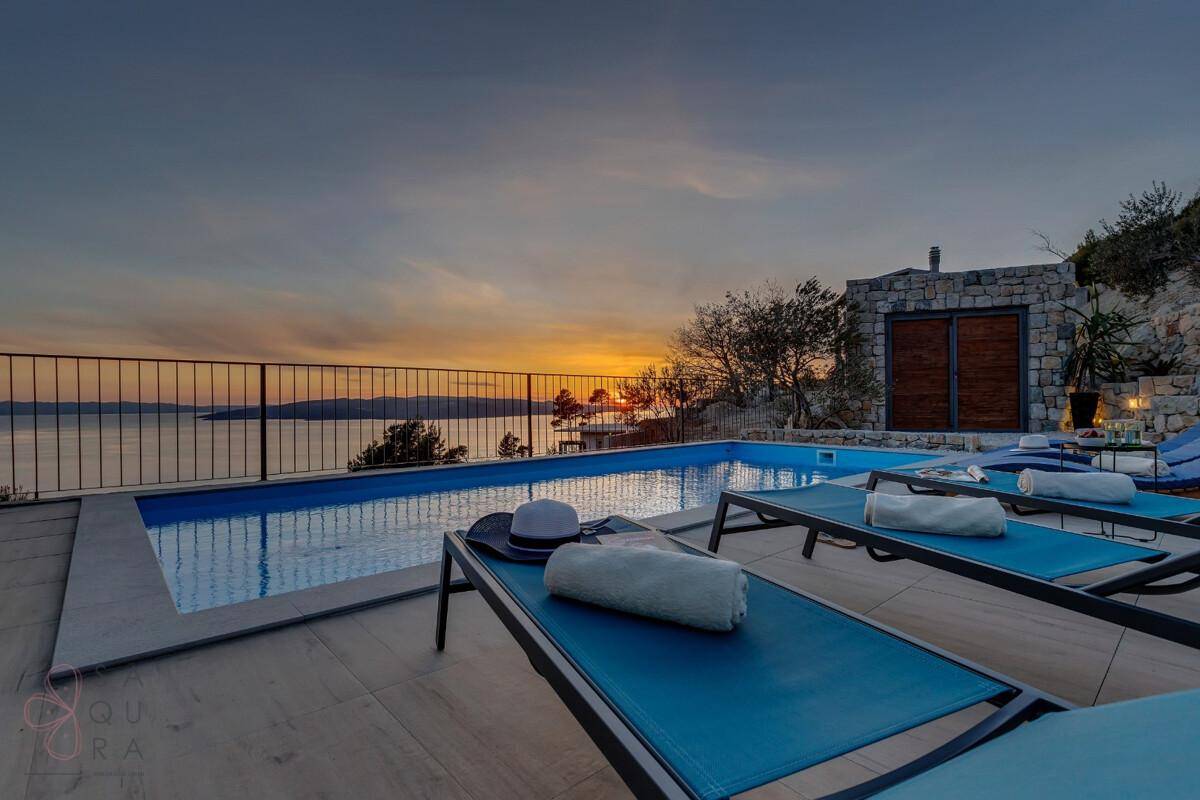 Entspannender Poolbereich bei Sonnenuntergang mit Liegestühlen und atemberaubendem Meerblick.