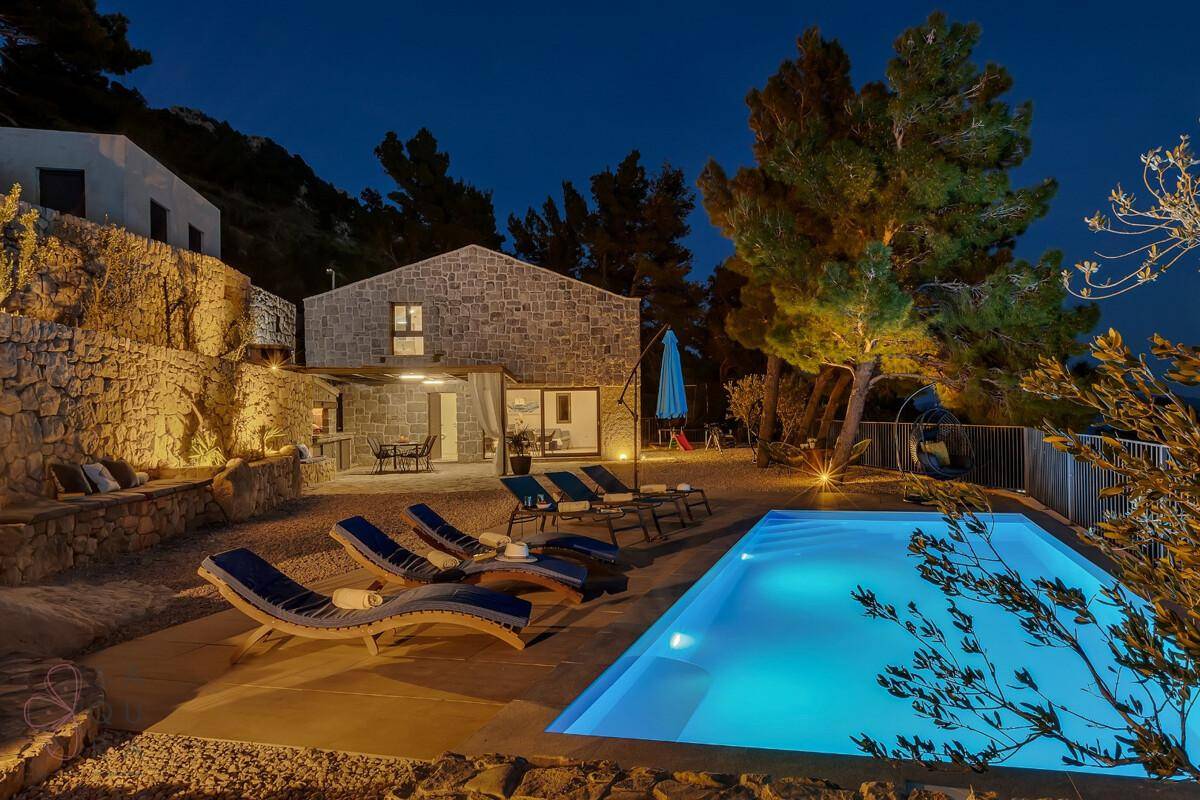 Beleuchteter Poolbereich bei Nacht mit Liegestühlen und stimmungsvoller Atmosphäre.