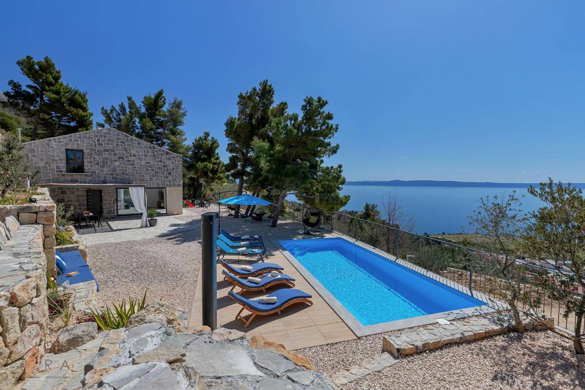 Sonniger Poolbereich mit bequemen Liegestühlen und weitem Blick auf das glitzernde Meer.