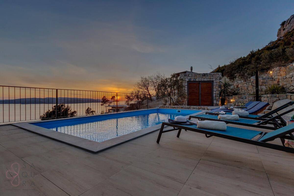 Entspannender Poolbereich bei Sonnenuntergang mit Liegestühlen und atemberaubendem Meerblick.
