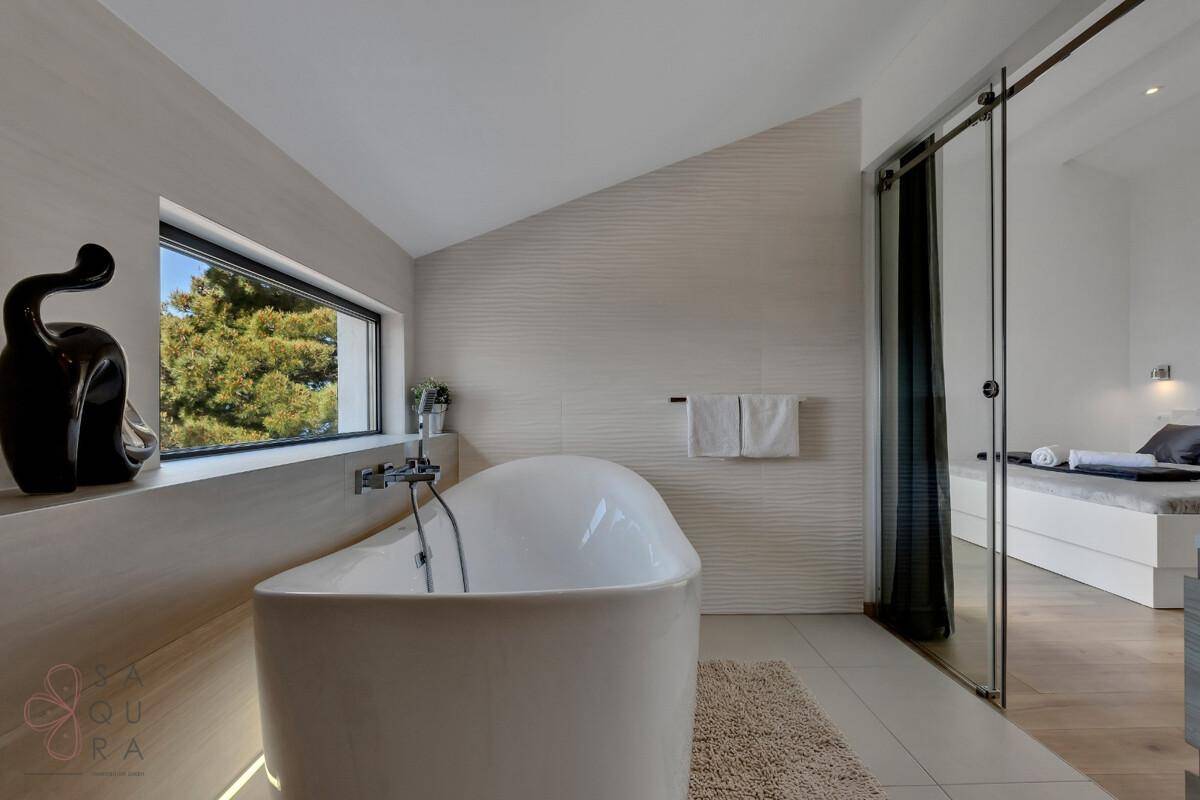 Modernes Badezimmer mit freistehender Badewanne und Dachschräge, direkt vom Schlafzimmer zugänglich.
