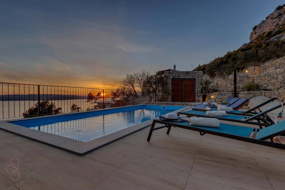 Entspannender Poolbereich bei Sonnenuntergang mit Liegestühlen und atemberaubendem Meerblick.