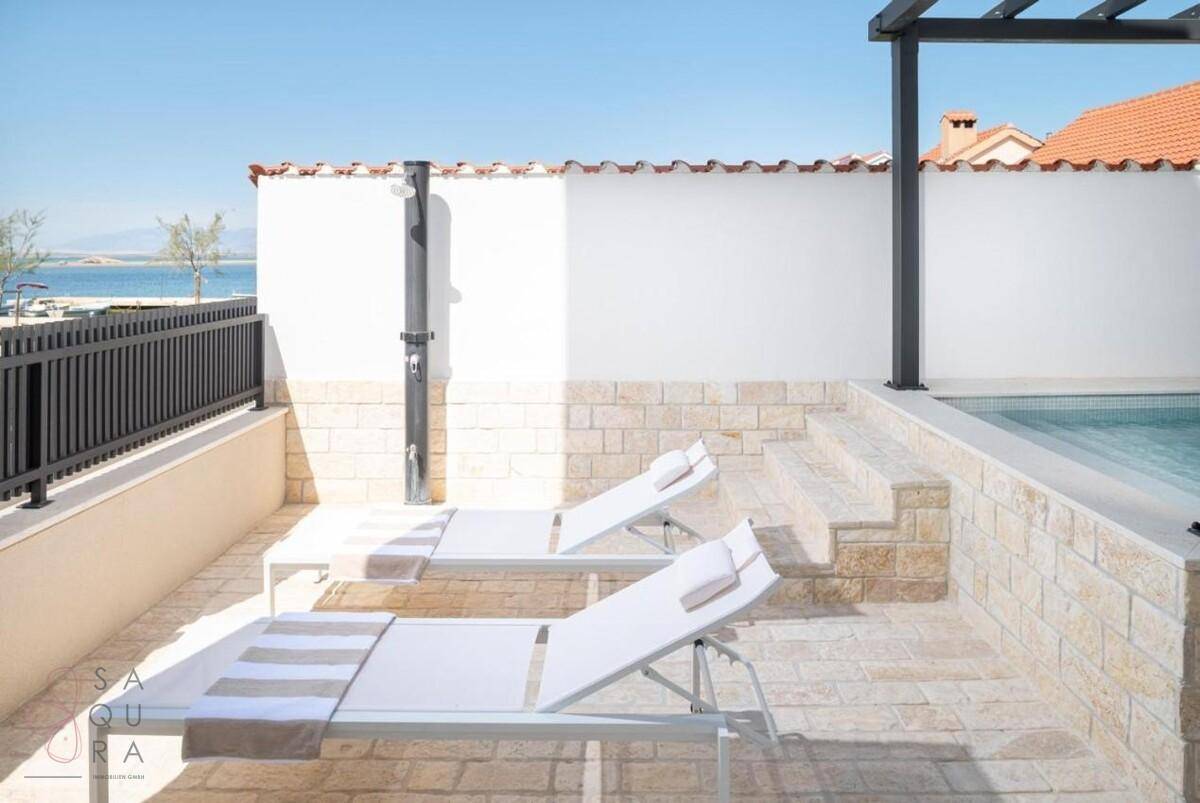 Sonniger Terrassenbereich mit bequemen Liegen, Außendusche und Zugang zum Pool.