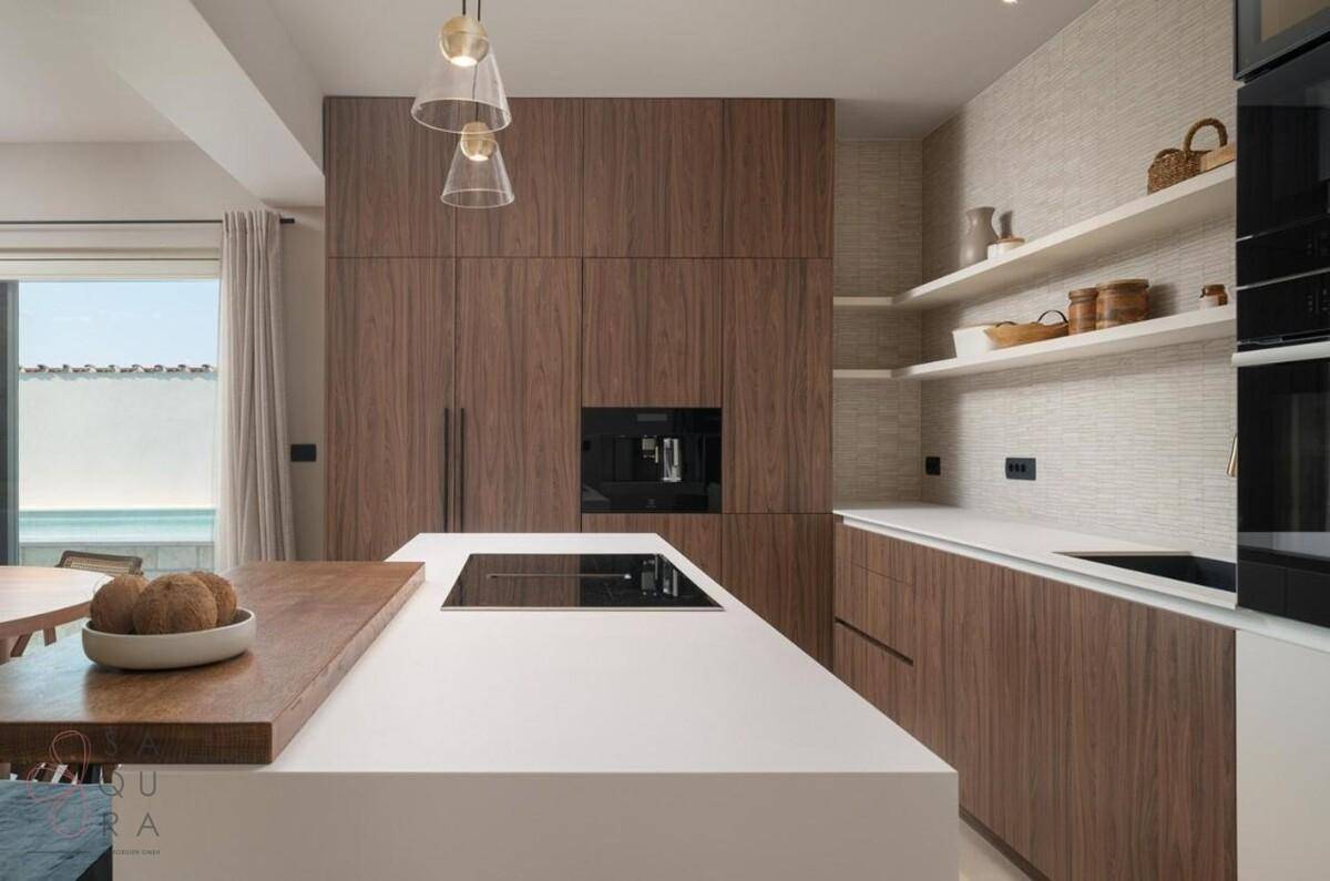 Moderne Holzküche mit weißen Arbeitsplatten, integrierten Geräten und Blick auf den Pool.
