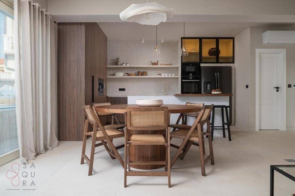 Offener Wohn- und Essbereich mit Holztisch und moderner Küche im Hintergrund.