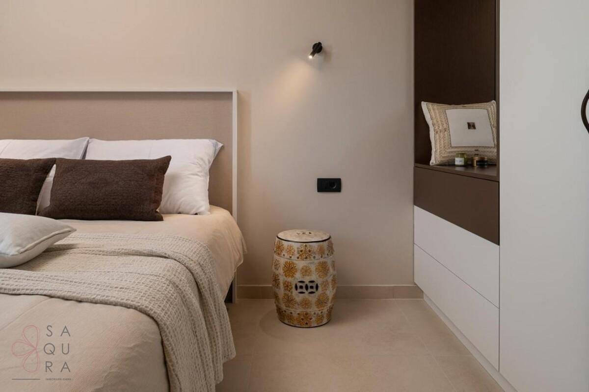 Schlafzimmer mit beigem Bett, dekorativem Beistelltisch und integrierten Schränken für Stauraum.