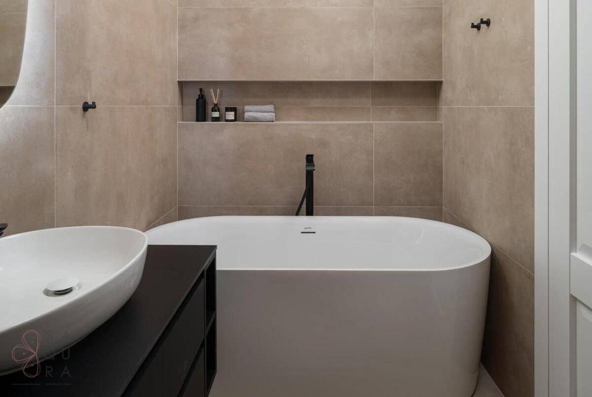 Modernes Badezimmer mit freistehender Badewanne, Aufsatzwaschbecken und beigen Fliesen an den Wänden.