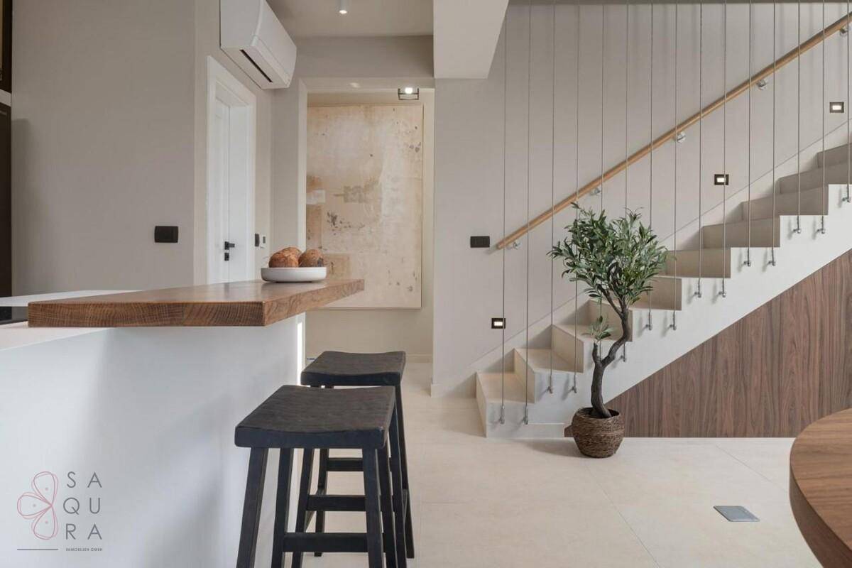 Offener Wohnbereich mit Frühstücksbar, modernen Hockern und einer stilvollen Treppe im Hintergrund.
