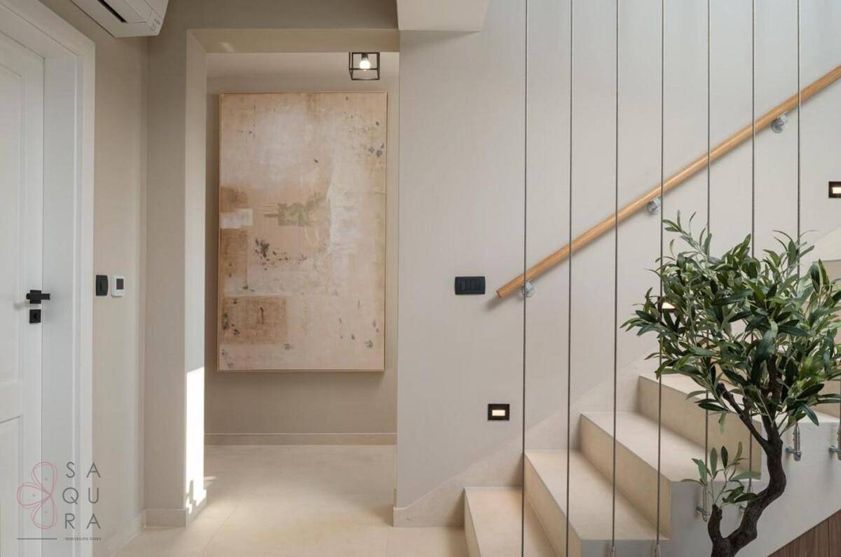 Heller Flur mit eleganter Treppe, minimalistischer Dekoration und einer dekorativen Olivenpflanze.