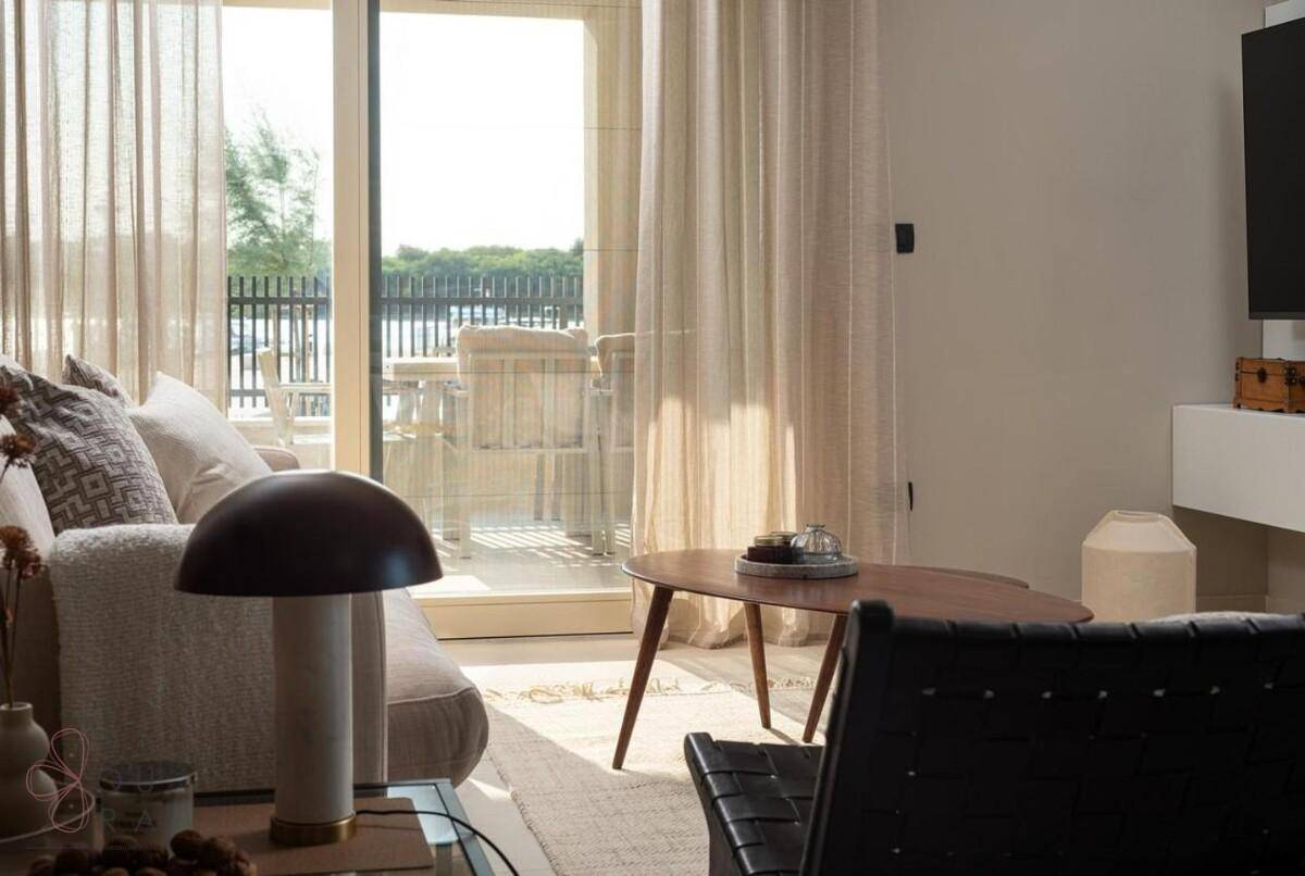 Sonniges Wohnzimmer mit Blick auf eine Außenterrasse und das glitzernde Wasser, ideal zum Entspannen.