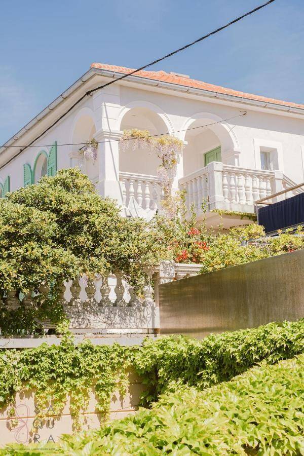 Detailansicht der Villa mit üppiger Vegetation, Balkon und traditionellen Fensterläden in Grün.