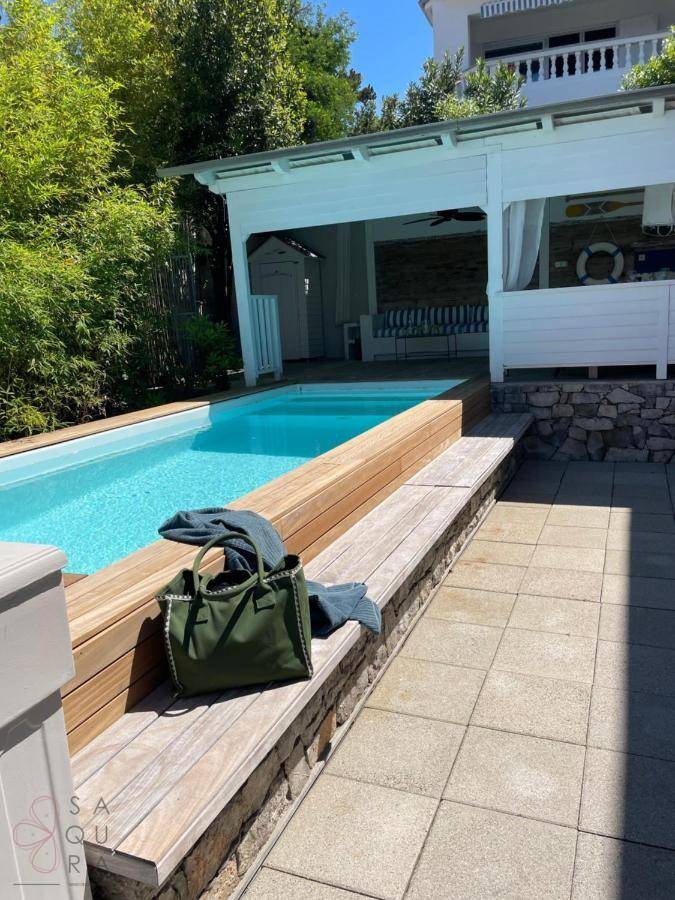 Moderner Poolbereich mit Holzdeck, Liegeflächen und überdachtem Sitzbereich.