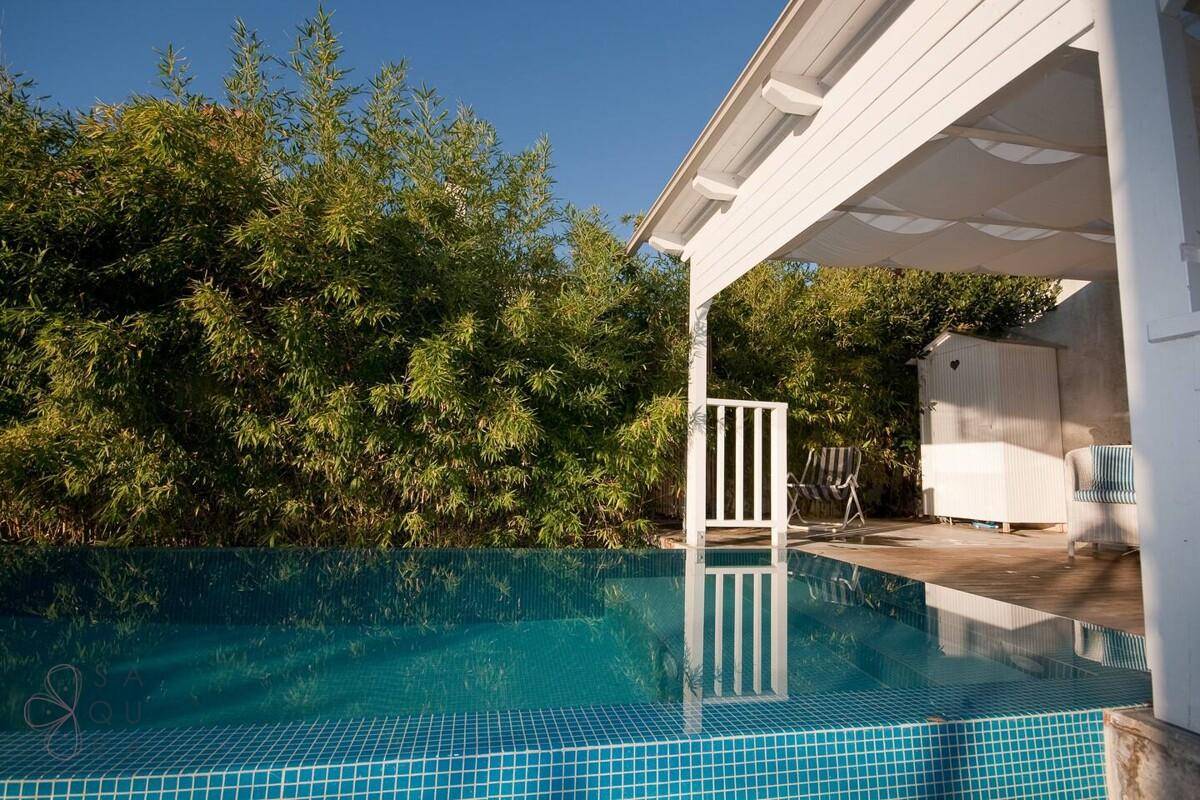 Blauer Pool umgeben von üppigem Grün und einer überdachten Terrasse.