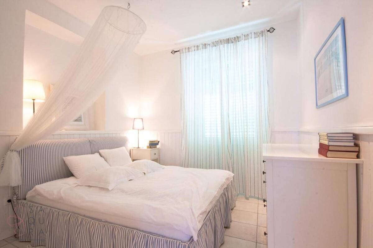 Helles Schlafzimmer mit gestreiftem Bett, weißen Möbeln und Fenster mit Vorhängen.