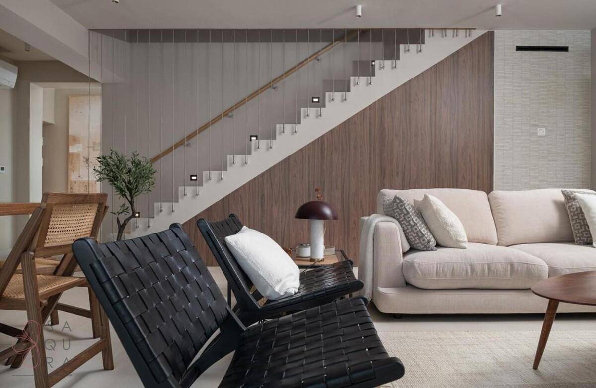 Gemütlicher Wohnbereich mit beigem Sofa, modernen Sesseln und einer eleganten Treppe im Hintergrund.