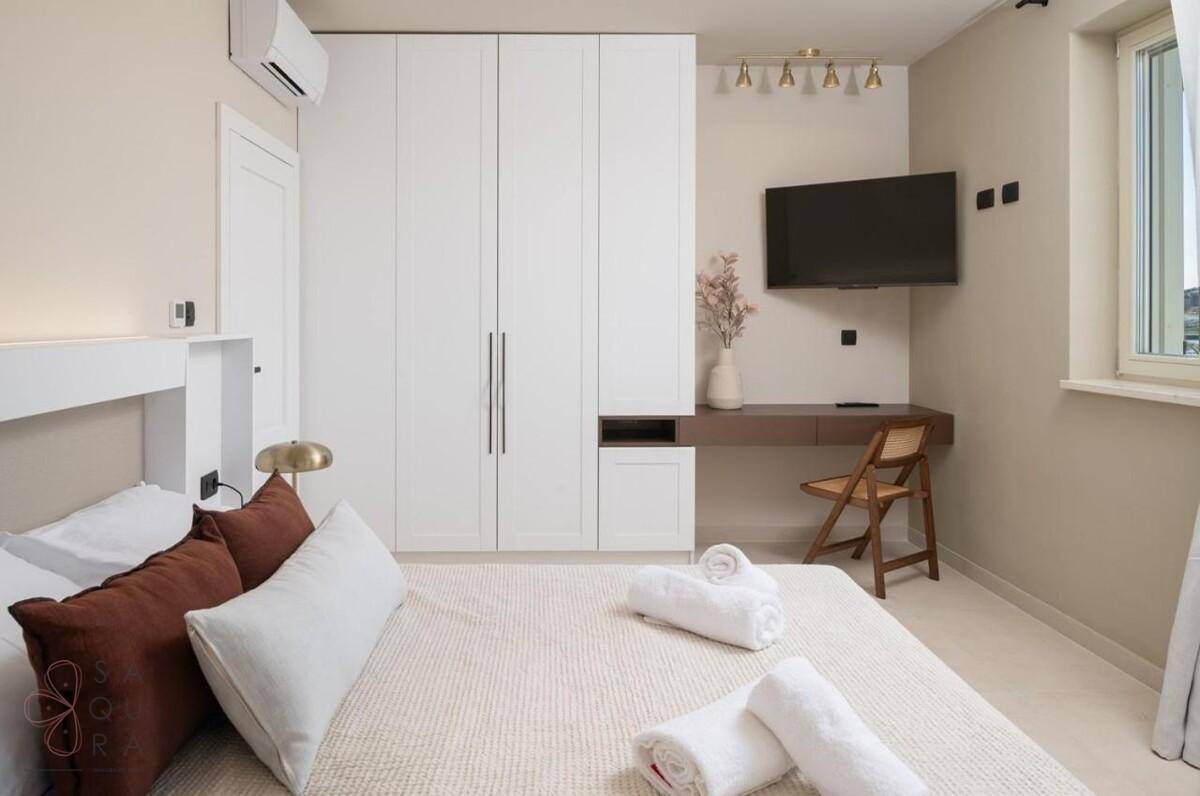Modernes Schlafzimmer mit großem Bett, Einbauschränken, Schreibtisch und Wandfernseher, sehr hell.