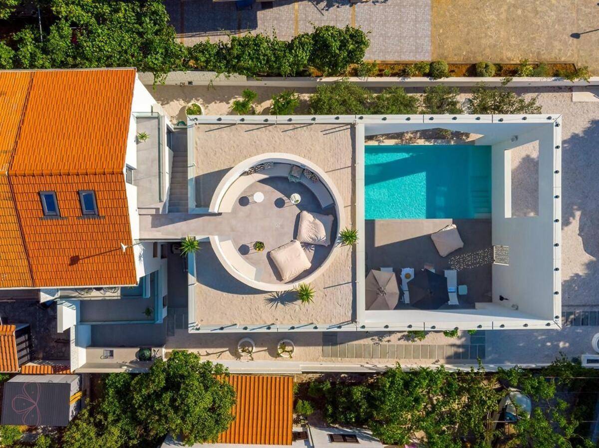 Vogelperspektive der modernen Villa mit Pool, Dachterrasse und umliegender Bebauung.