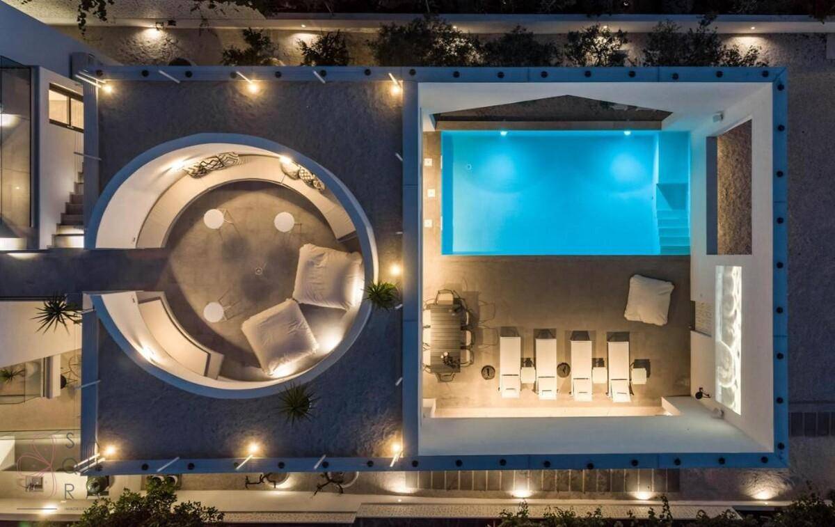 Luftaufnahme der beleuchteten Villa mit Pool und runder Lounge-Terrasse bei Nacht.