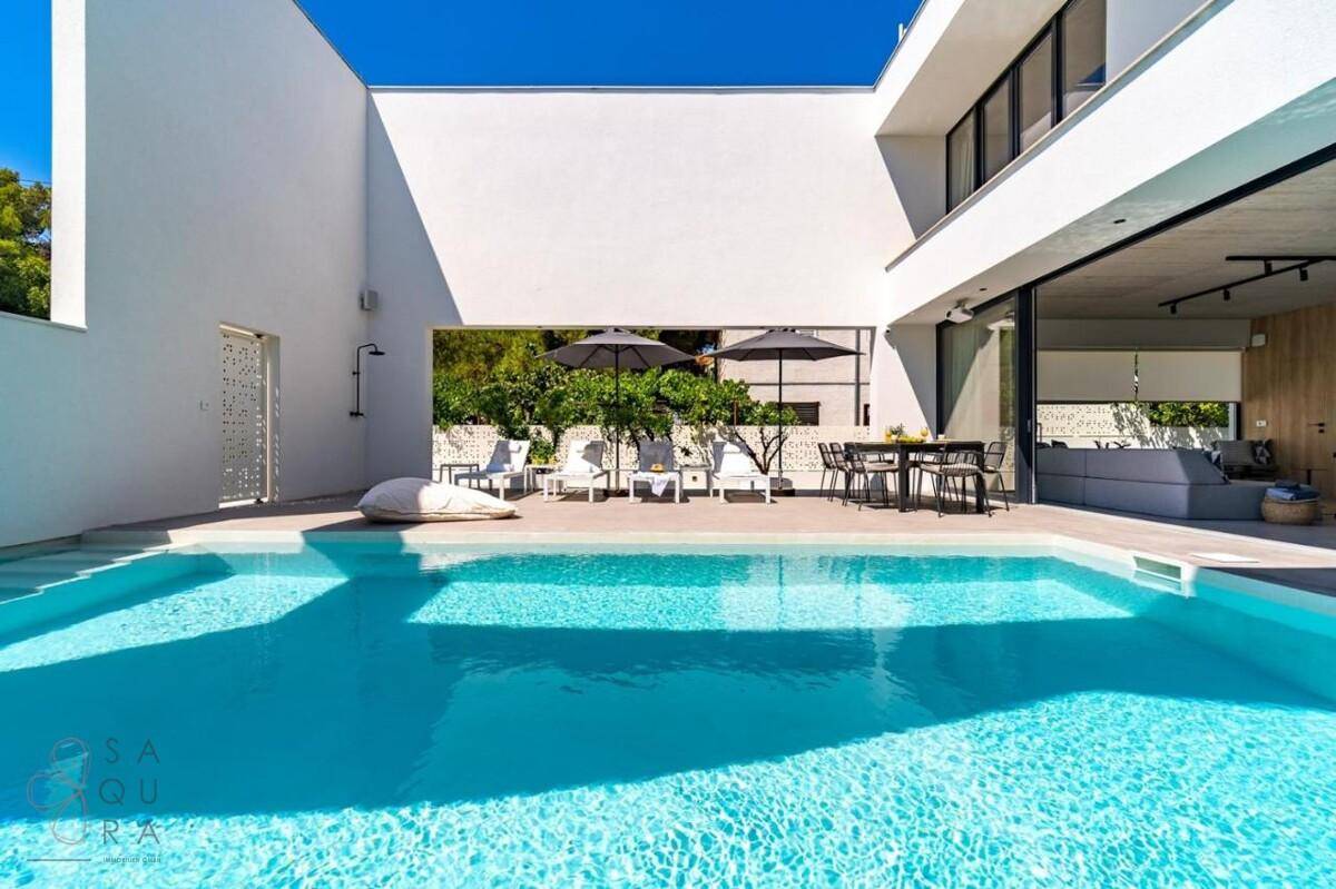 Geräumiger Poolbereich mit Liegestühlen, Essbereich und moderner Außendusche in sonniger Umgebung.