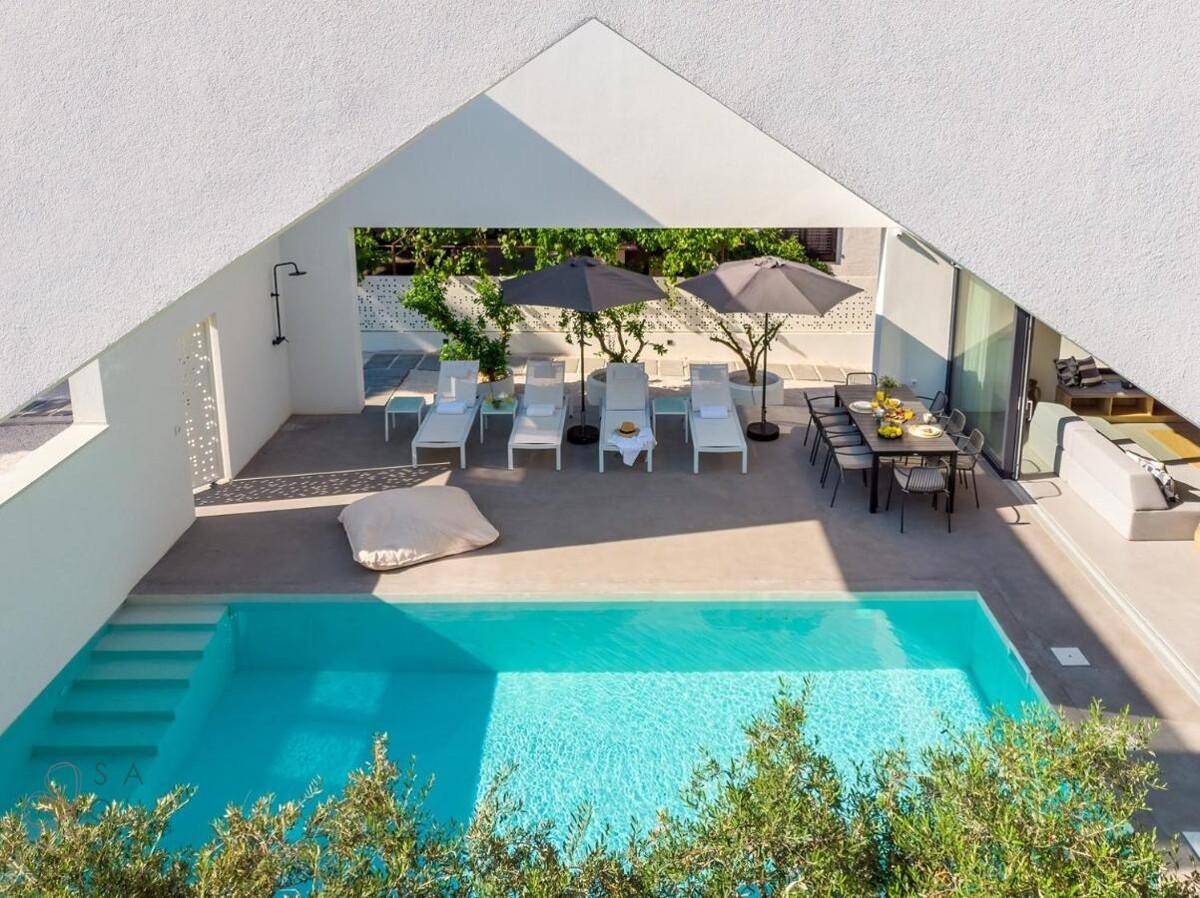 Geräumiger Poolbereich mit Liegestühlen, Essbereich und moderner Außendusche unter Sonnenschirmen.