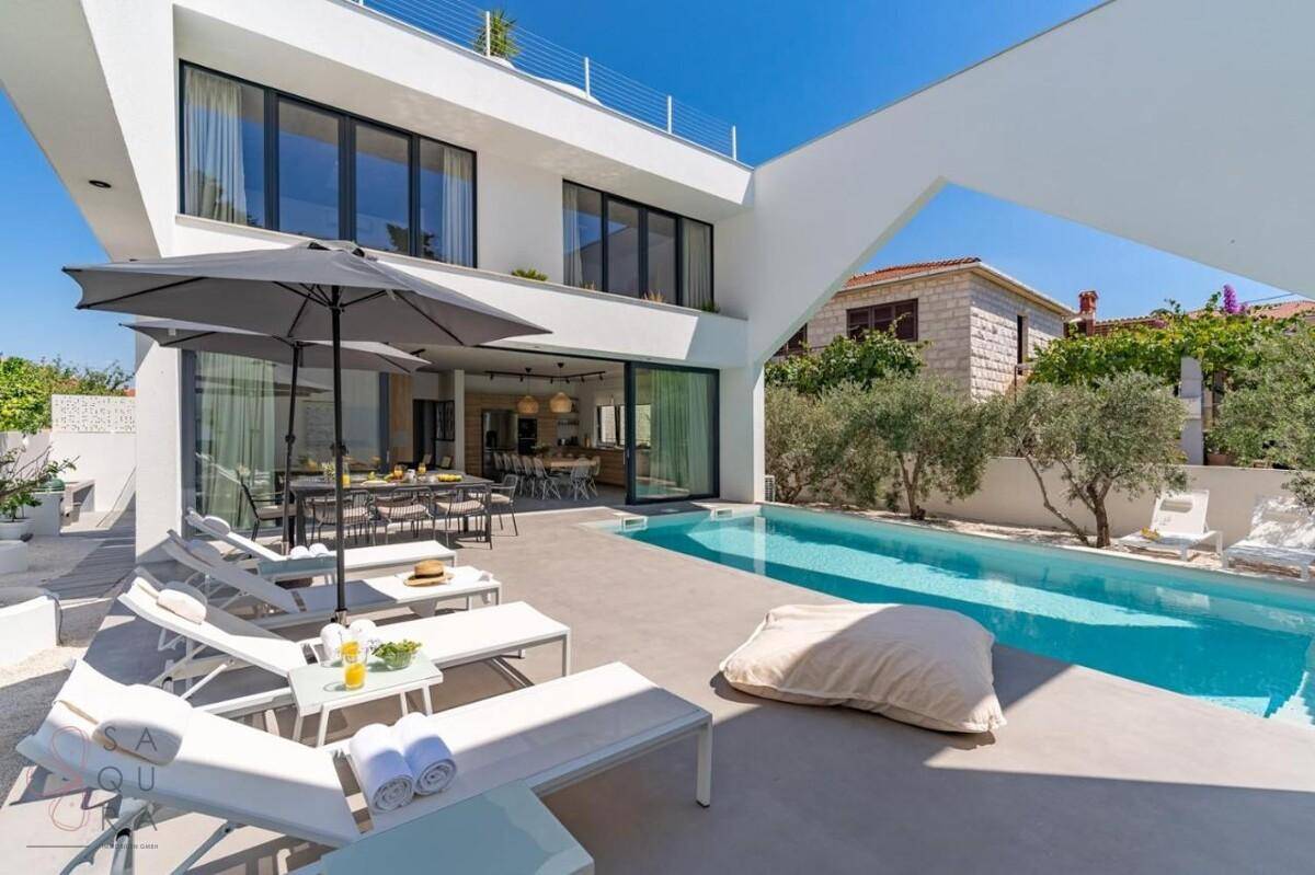 Moderne Villa mit großem Pool, Sonnenterrasse und Essbereich im Freien unter Sonnenschirmen.