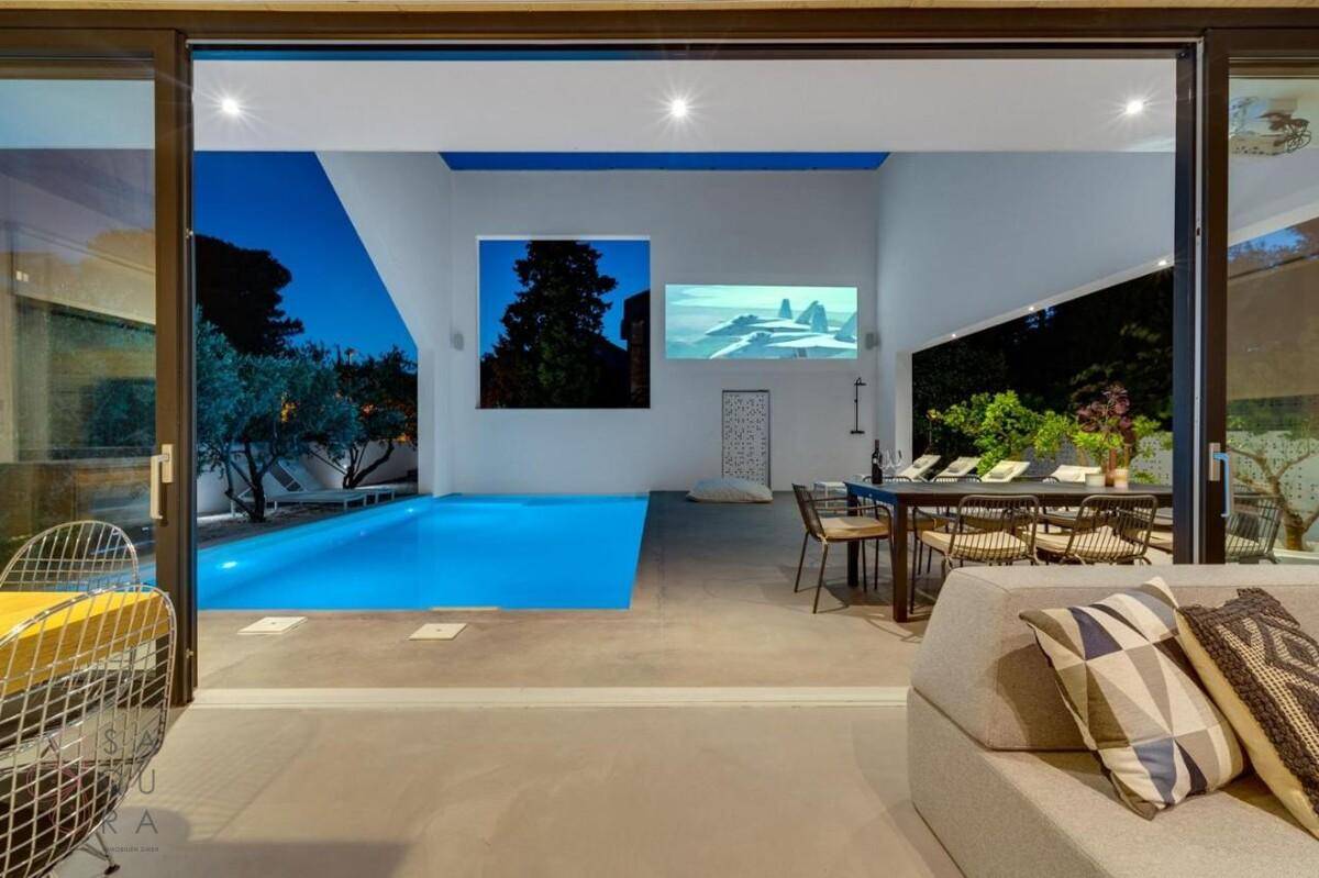 Gemütlicher Wohnbereich mit Blick auf den beleuchteten Pool und Außenbereich bei Nacht.