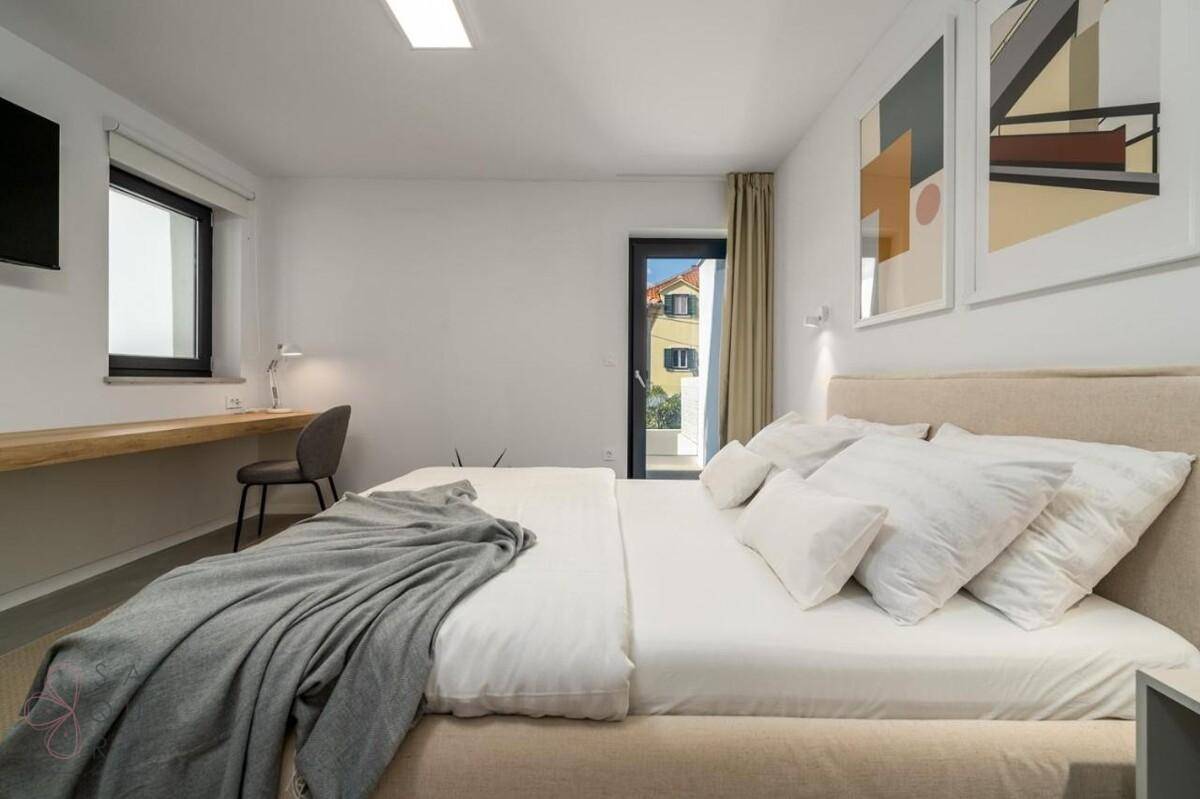 Helles Schlafzimmer mit Doppelbett, Schreibtisch und Zugang zu einem kleinen Balkon.