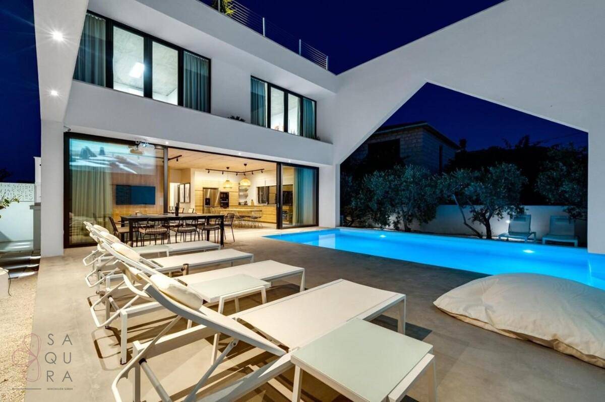 Moderne Villa mit beleuchtetem Pool, Terrasse und Lounge-Bereich bei Nacht.