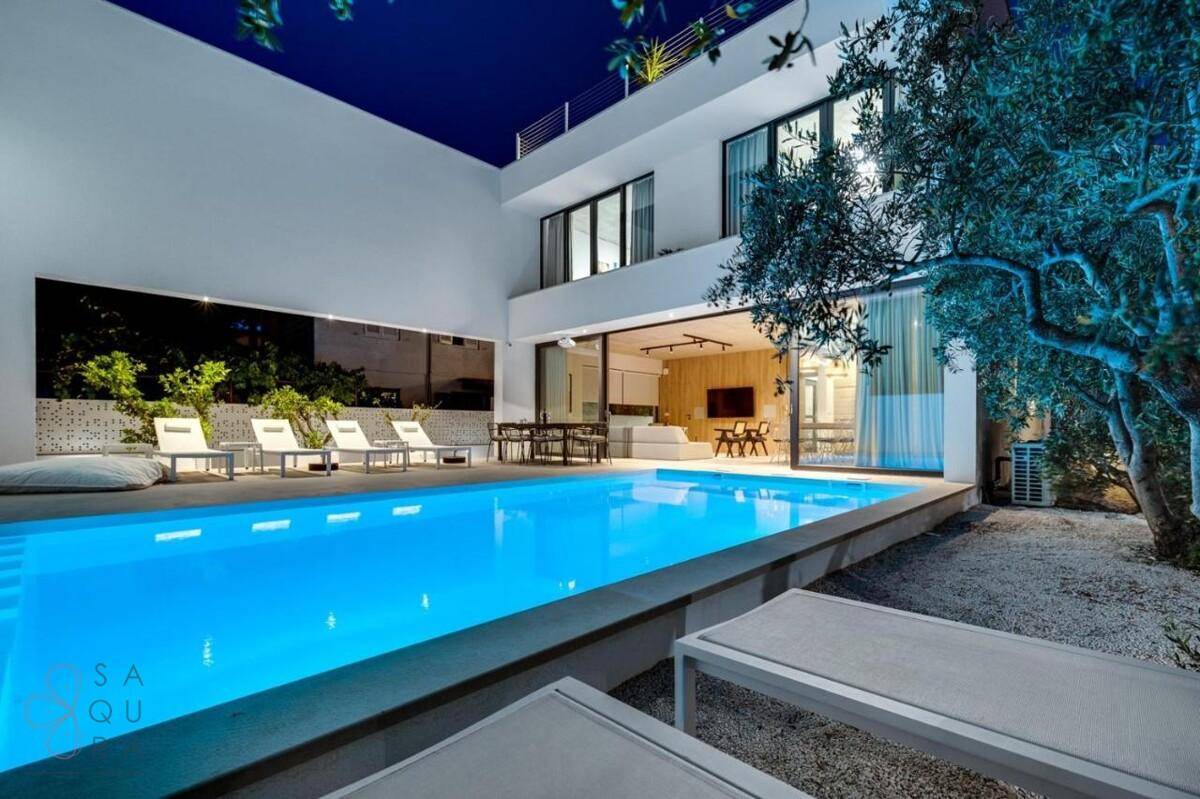 Moderne Villa mit beleuchtetem Pool, Terrasse und Lounge-Bereich bei Nacht.
