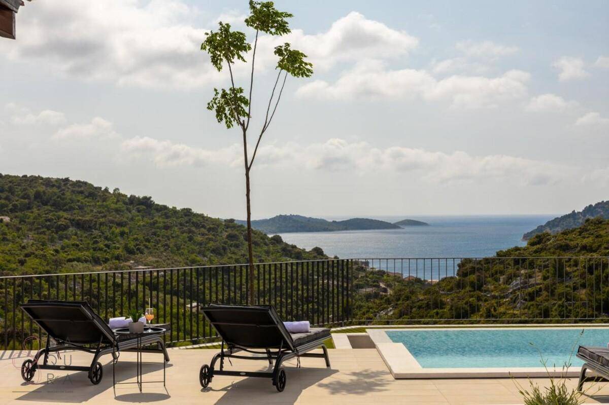Entspannender Poolbereich mit Liegestühlen und weitem Blick auf das Meer und die umliegende grüne Landschaft.