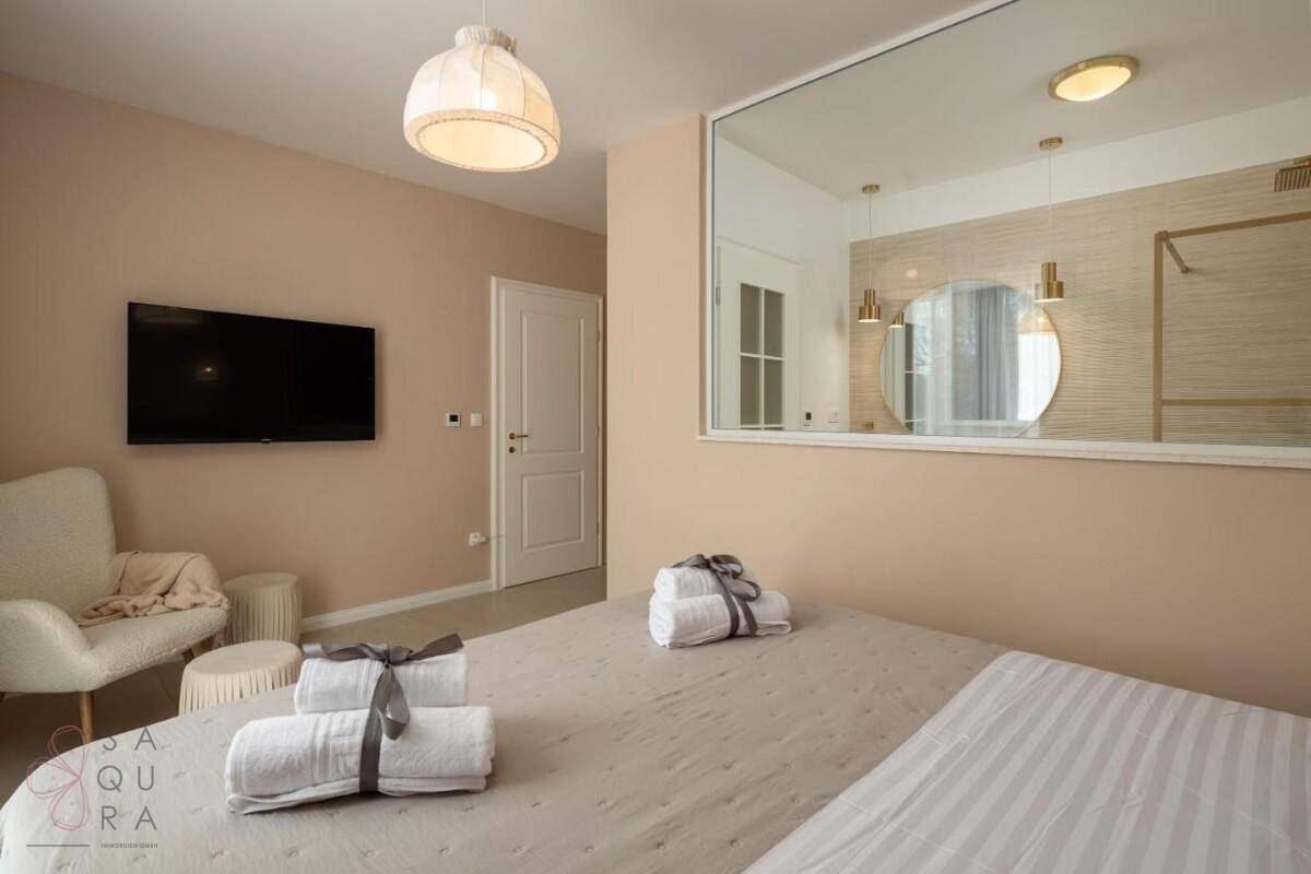 Modern eingerichtetes Schlafzimmer mit Flachbildfernseher und einem großen Spiegel, der den Raum erweitert.