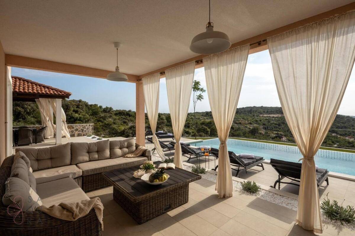 Gemütliche überdachte Terrasse mit Lounge-Möbeln und direktem Blick auf den Pool und das Meer.