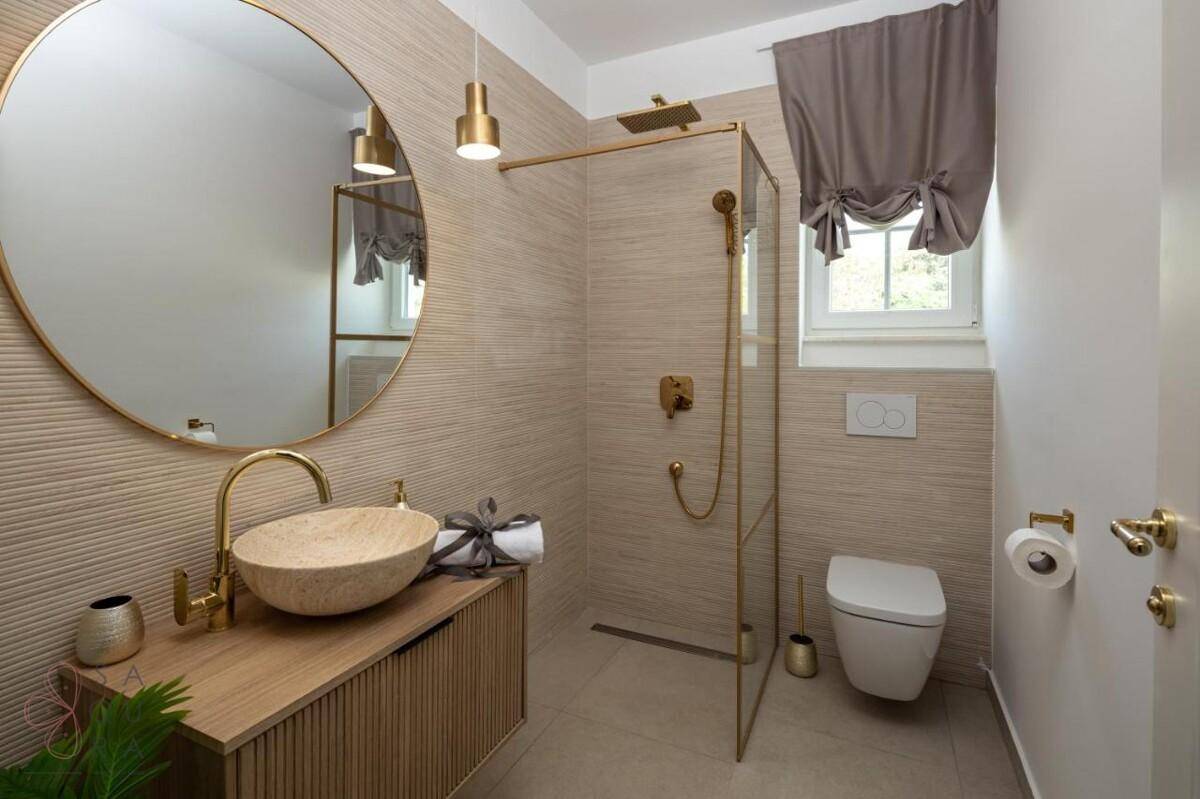Elegantes Badezimmer mit modernem Design, runden Spiegeln, begehbarer Dusche und goldenen Armaturen.