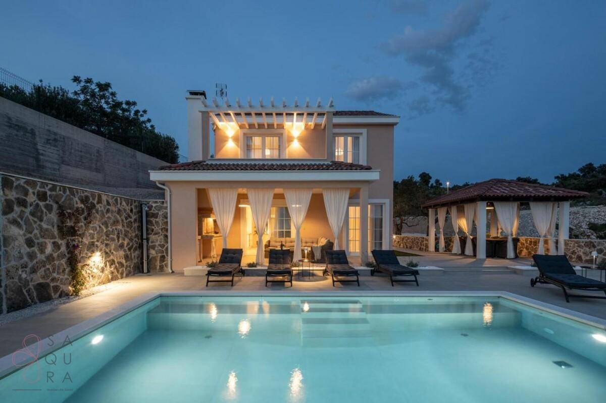 Moderne Villa bei Nacht mit beleuchtetem Pool und Steinfassade, umgeben von mediterraner Natur.