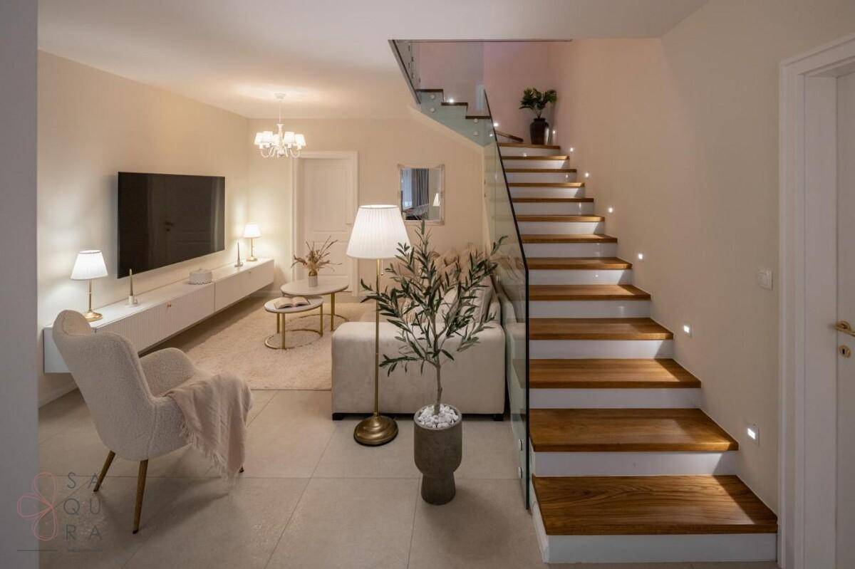 Geräumiges Wohnzimmer mit bequemen Sitzgelegenheiten und einer eleganten Holztreppe mit Glasgeländer.