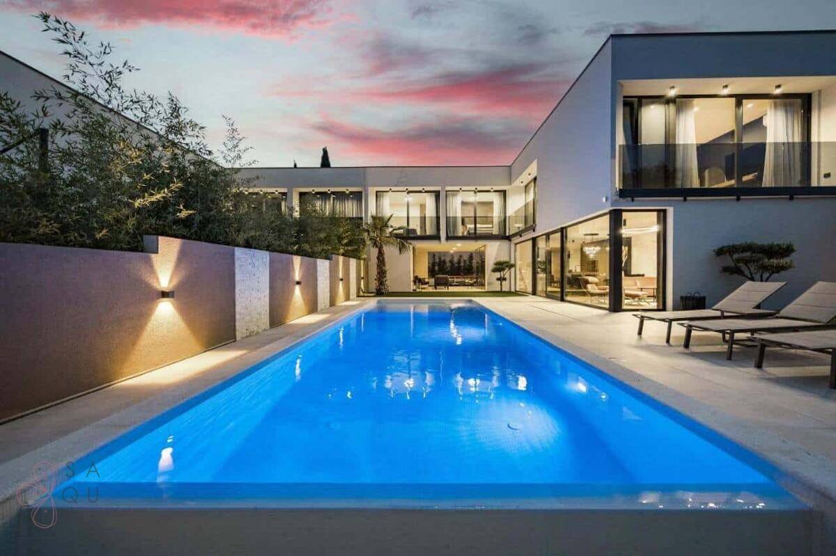 Elegante moderne Villa mit langem, beleuchtetem Pool und stilvoller Außenbeleuchtung.