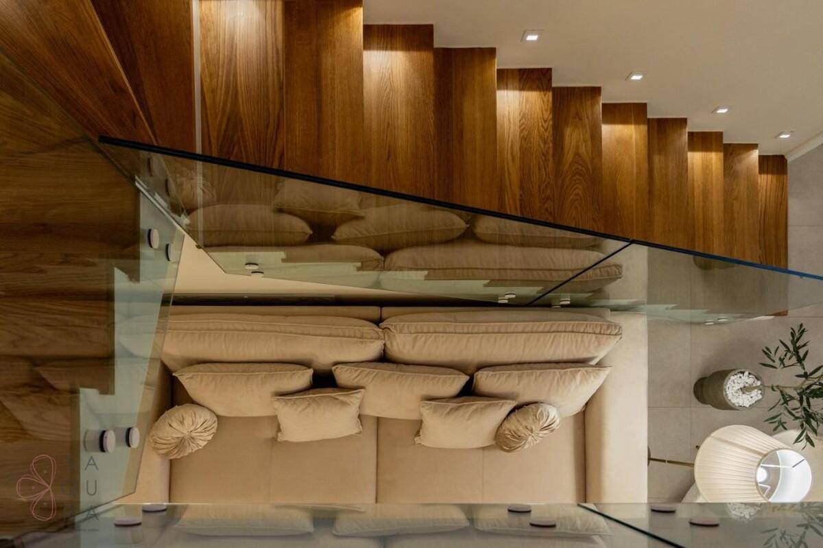 Detailaufnahme der modernen Holztreppe mit Glasgeländer und einem bequemen Sofa im Wohnbereich.