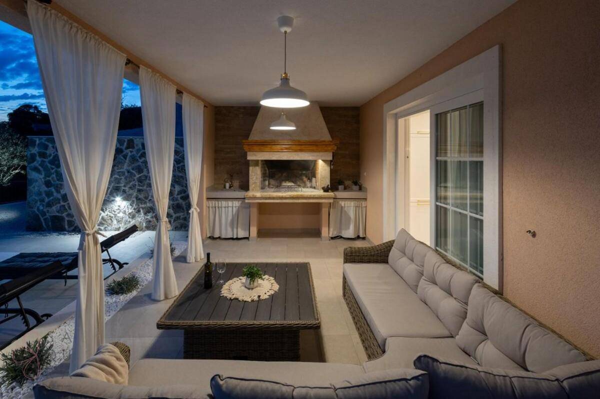 Überdachte Terrasse mit bequemen Lounge-Möbeln und einem integrierten Grillbereich, ideal für Abende im Freien.